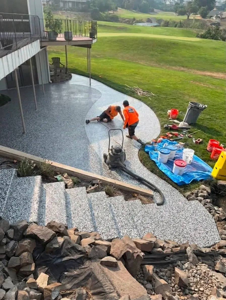 A contractor's patio job photo previewed in Domino epoxy flake, darker in the shade of the house and deck and lighter on the sunny curve