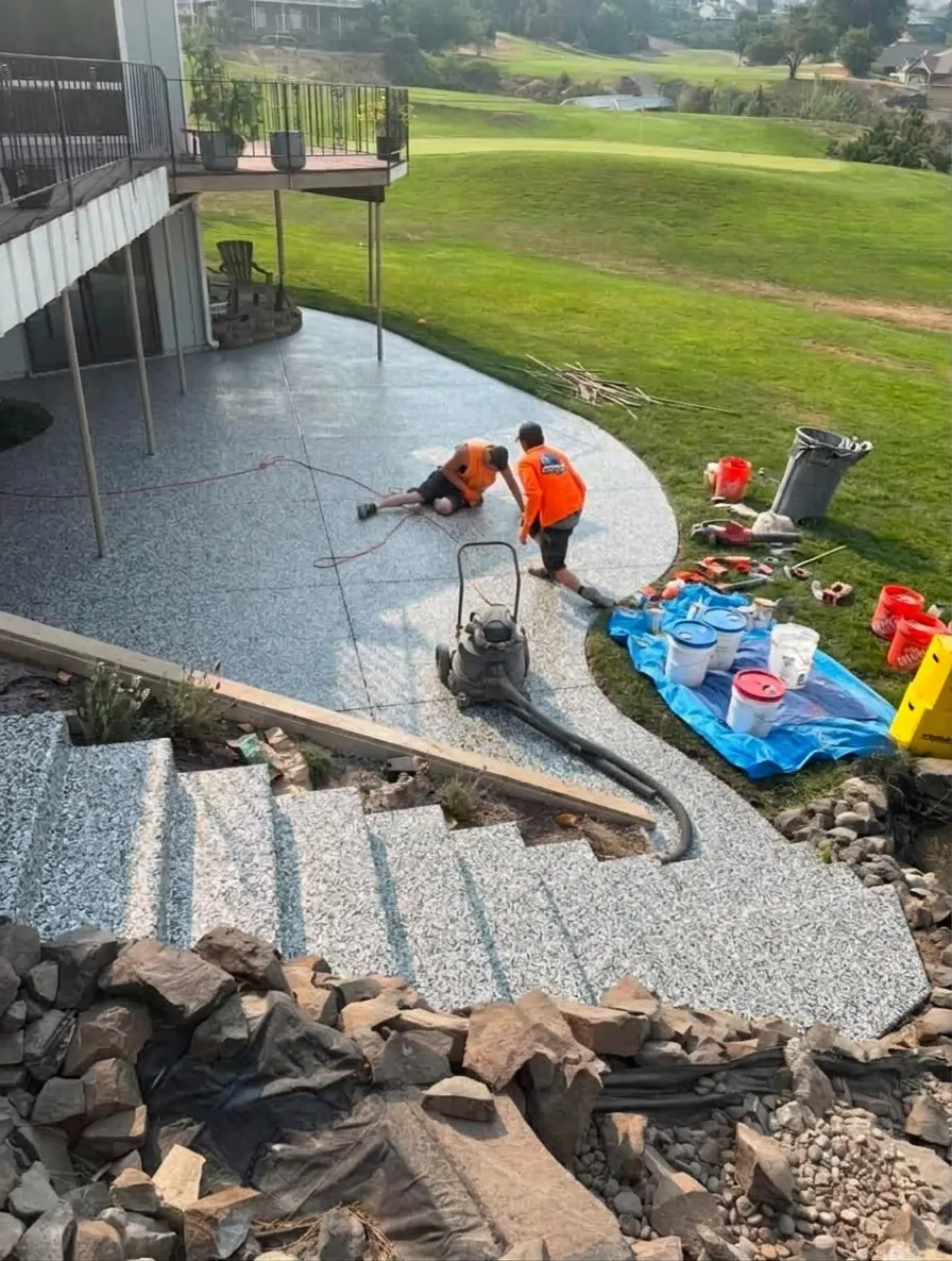 AI preview: A contractor's concrete patio and steps with the crew prepping the slab, then the same photo previewed in a gray flake finish